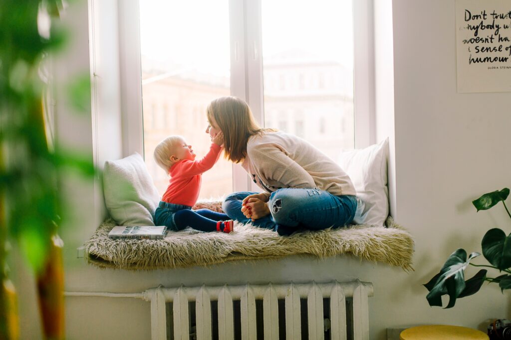 baby touching moms face as they sit by a window