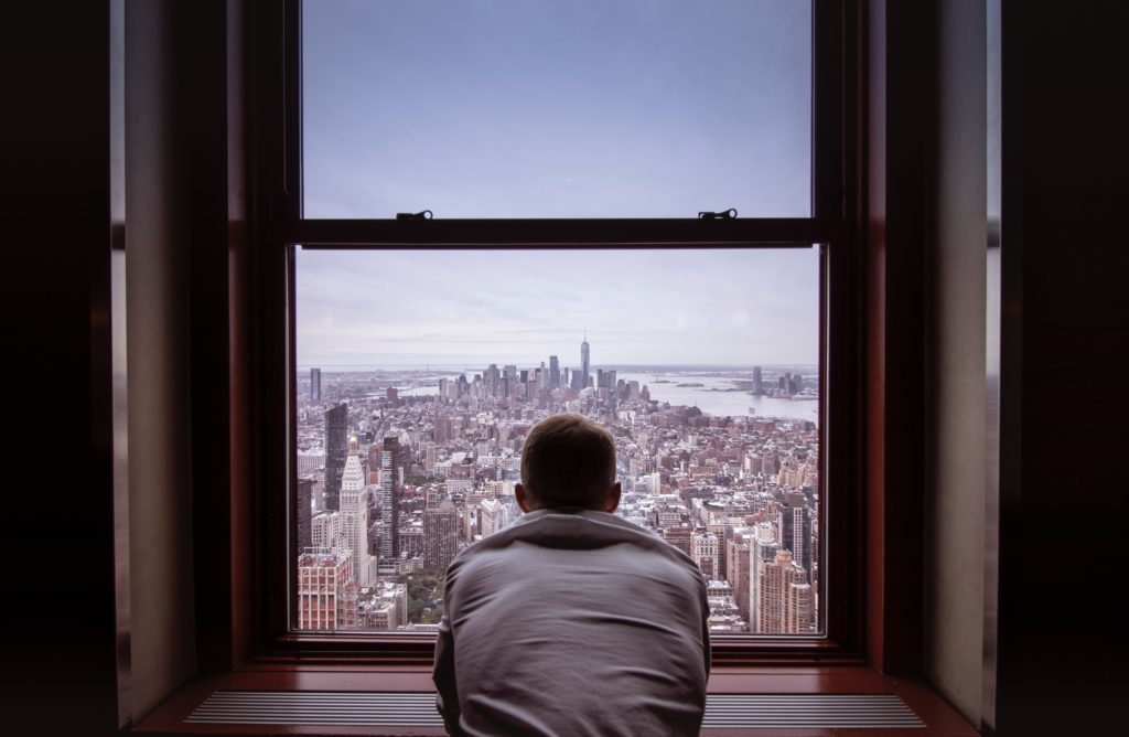man looking out window at city